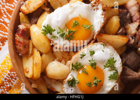 La cuisine autrichienne : pommes de terre sautées avec de la viande, œufs et bacon close-up dans un bol en bois horizontale vue du dessus. Banque D'Images