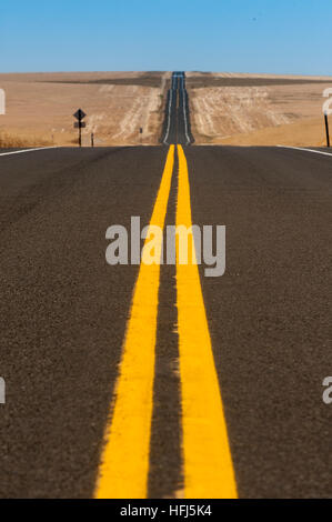 Larges lignes jaunes sur une autoroute à deux voies blacktop qui traverse les champs de blé doré. Banque D'Images