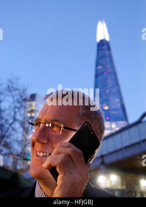 Smiling city man businessman outdoors parle de bonnes nouvelles sur son iPhone 7 plus au crépuscule avec 'Le tesson' tour en arrière-plan London SE1 UK Banque D'Images