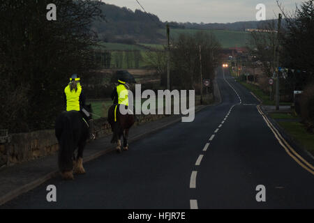 Deux cavaliers portant des vêtements haute visibilité sur route rurale sombre Banque D'Images