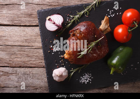Jarret de porc au four et légumes frais close up sur un conseil d'ardoise sur la table horizontale vue du dessus. Banque D'Images