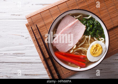 La nourriture asiatique : nouilles ramen dans un bouillon avec du porc, des légumes et d'oeuf dans un bol de près. Vue supérieure horizontale Banque D'Images