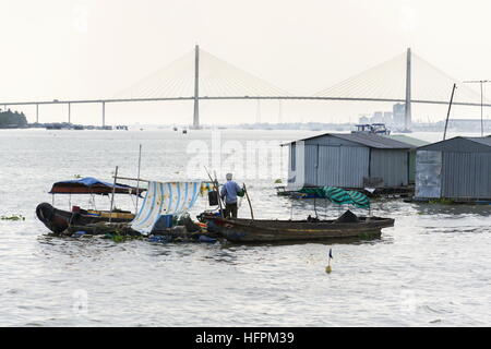 L'homme navigue sur bateau ratty avec fish farm maisons radeau flottant sur le Mékong avec le pont Rach mieu à My Tho, Vietnam. Banque D'Images