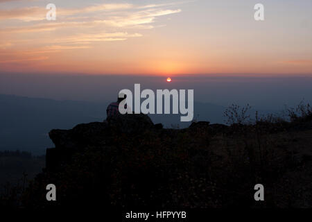 La silhouette d'un homme regardant un magnifique coucher de soleil depuis un sommet de montagne. Banque D'Images