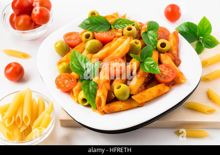 Assiette de pâtes penne décoré de tomates cerises, olives et d'herbes sur un plateau en bois Banque D'Images