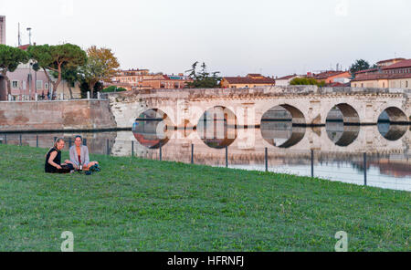 Méconnues des jeunes femmes avaient un pique-nique sur l'herbe en face de l'ancien pont sur le canal de la mer. Rimini, Italie. Banque D'Images