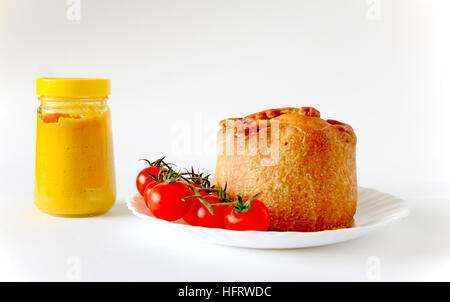 Un Melton Mowbray pork pie et tomates cerises sur une plaque blanche avec un pot de moutarde anglaise. Banque D'Images