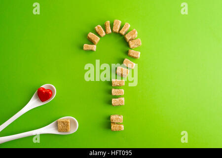 Brown Sugar cubes en forme de point d'interrogation sur fond de verdure et deux cuillères de blanc avec coeur sur l'un d'eux. Vue d'en haut. Pour régimes unhealty sweet addiction concept Banque D'Images