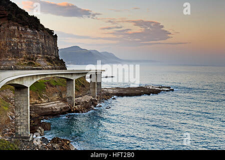 Vue latérale du pont sur la falaise la Grand Pacific Drive en Australie. Coucher du soleil sur l'océan pacifique lumineux de façon moteur de tourisme pittoresque vallonné face à l'autre. Banque D'Images