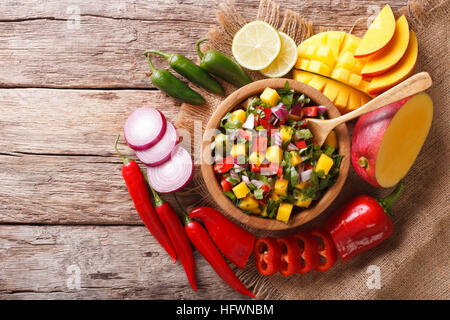 Salsa mexicaine à la mangue, la coriandre, les oignons et les piments forts close up dans un bol en bois et les ingrédients sur la table. Vue du dessus horizontale Banque D'Images