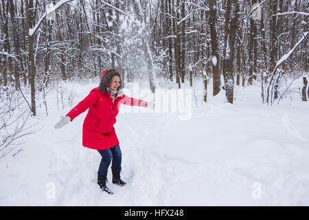 La haute vieille femme projette la neige dans le bois en manteau rouge Banque D'Images