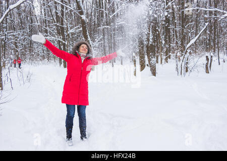 La haute vieille femme projette la neige dans le bois en manteau rouge Banque D'Images