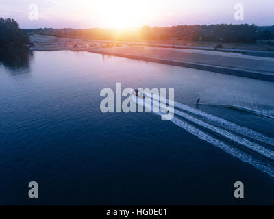 Vue aérienne de l'homme le ski nautique sur le lac derrière bateau. Man wakeboarding au coucher du soleil. Banque D'Images