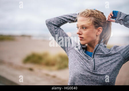 Close up of young female runner immobiliser des cheveux avant une exécution. Femme de remise en forme sportive de plein air à l'entraînement sur route. Banque D'Images