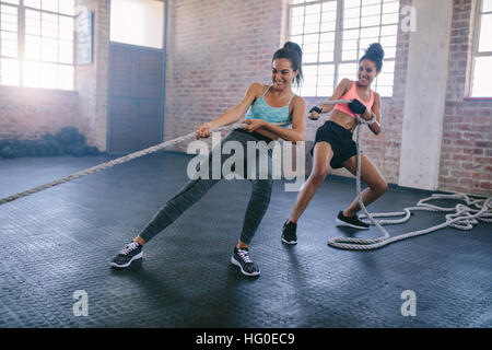 Plan de deux jeunes femmes fortes faisant des exercices de traction de corde dans une salle de gym. femmes de fitness tirant la corde au gymnase et souriant. Banque D'Images