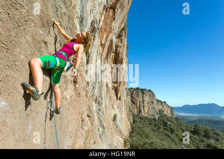 Les jeunes female Rock Climber hanging sur mur vertical Banque D'Images