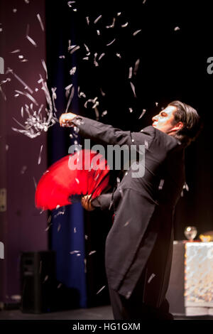 Un magicien habillé formellement un ventilateur rouge ondes et disperse les confettis tout en effectuant un tour à un Huntington Beach, CA, le théâtre. Banque D'Images