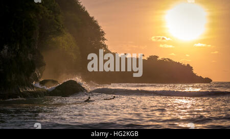 Les enfants surfent sur les vagues dans le coucher du soleil la lumière, Belle Baie Cristal, Nusa Penida Bali Banque D'Images