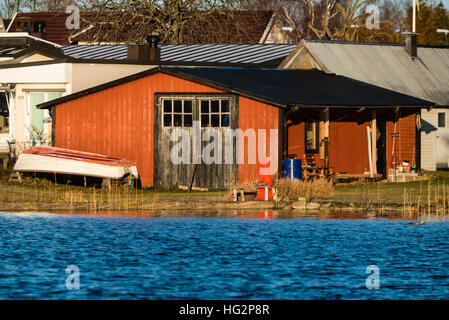 En bois rouge d'un hangar à bateaux comme vu de la mer. Les portes fermées et les petits chaloupe sur terre à l'extérieur. Calme et ensoleillé. Banque D'Images