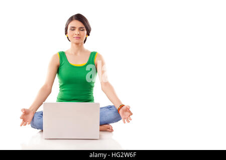 Jeune femme en méditant posent avec les yeux fermés et les jambes croisées, tout en faisant face à un ordinateur portable à l'avant. Isolé sur fond blanc Banque D'Images