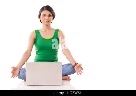 Jeune femme en méditant posent avec les yeux fermés et les jambes croisées, tout en faisant face à un ordinateur portable à l'avant. Isolé sur fond blanc Banque D'Images