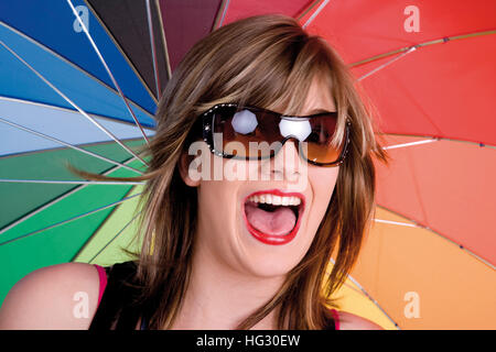 Jeune femme portant des lunettes de soleil permanent, sous un parapluie multicolore Banque D'Images