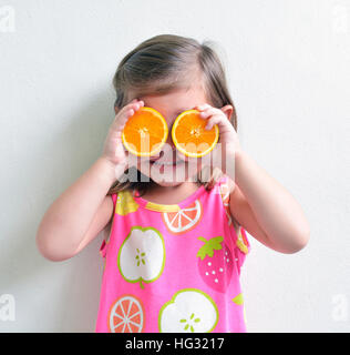 Young Girl holding tranches oranges au-dessus des yeux Banque D'Images