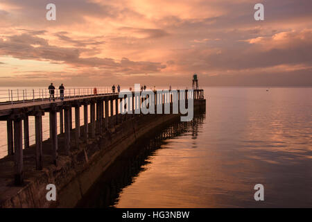 Au coucher du soleil, les gens et pier sont découpé sur le spectaculaire, ciel et mer rouge vif - Whitby, North Yorkshire, Angleterre. Banque D'Images