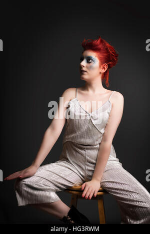 Red haired model with blue maquillage créatif portant robe d'argent, assis sur le tabouret en bois Banque D'Images