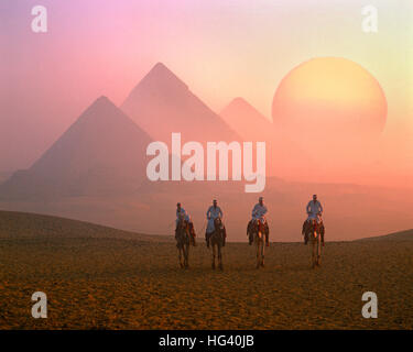 Quatre coureurs de chameau, les Pyramides et le soleil levant, Giza, Le Caire, Egypte Banque D'Images