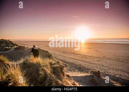 Un couple sur une plage en regardant vers le coucher du soleil en hiver Banque D'Images