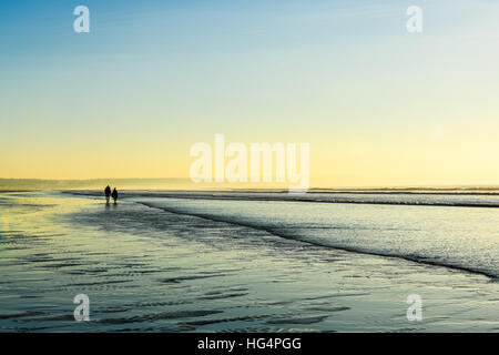 Un jeune couple amoureux se tenant la main sur une plage au coucher du soleil. Banque D'Images