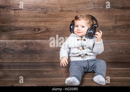 Baby Boy smiling sur fond de bois avec bluetooth/casque sans fil. Banque D'Images