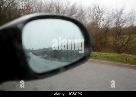 Aile de voiture miroir reflétant la route derrière le gris humide awet jour. Banque D'Images