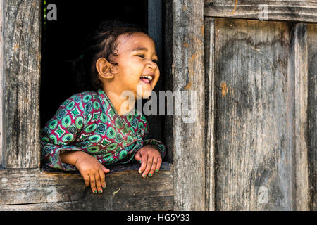 Portrait de rire petite fille, Upper Marsyangdi vallée, regardant par une fenêtre, Bagarchap, District de Manang, Népal Banque D'Images