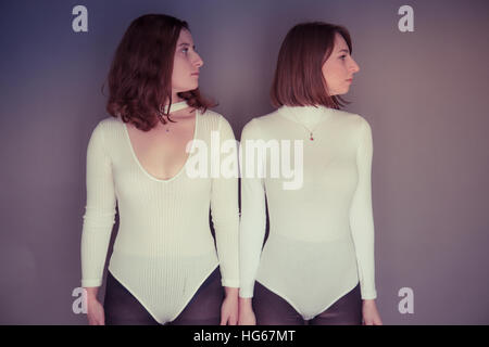 Doppelganger / Alter-ego photoshoot à thème : deux jeunes femmes les filles portant des vêtements correspondant permanent s'est réuni l'écho correspondant à chaque mise en miroir d'autres posent et d'expression physique - regardant à droite Banque D'Images