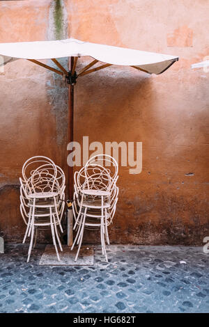 Un parasol et des chaises métalliques empilés à l'extérieur d'un restaurant dans la zone Trastevere de Rome, Italie. Banque D'Images