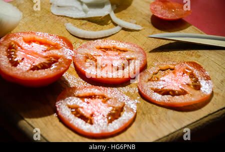 Photographie d'un couteau, les tranches de tomate et l'oignon sur une planche à découper en bois Banque D'Images