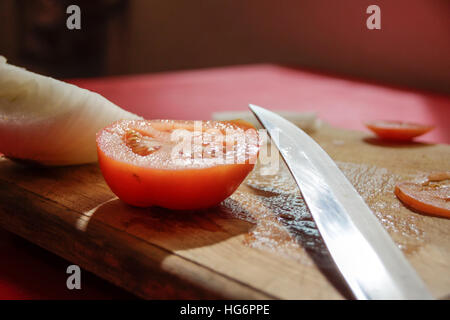 Photographie d'un couteau, les tranches de tomate et l'oignon sur une planche à découper en bois Banque D'Images