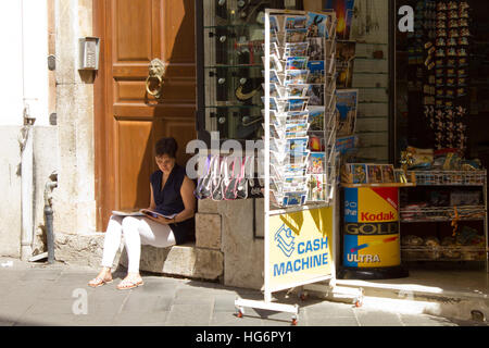 Femme assise à l'ombre par une chaude journée ensoleillée dans un Italien rue sicilienne Banque D'Images