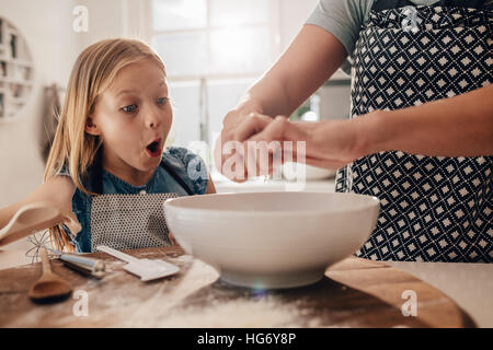 Excitée jeune fille avec la mère de préparer la pâte à cuire. Femme mains cuisine avec sa fille à la cuisine. Banque D'Images