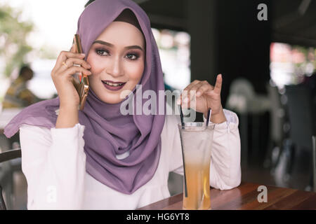 Belle jeune femme malais faisant un appel téléphonique au café avec visage souriant Banque D'Images