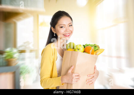 Young Asian woman holding shopping sac en papier rempli de fruits et légumes en magasin ou au café du marché . Banque D'Images