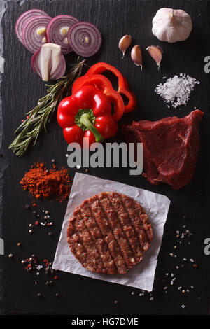 Burger de viande de boeuf haché cru escalopes steak avec des ingrédients sur le plateau. vertical Vue de dessus Banque D'Images