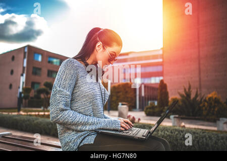 Young woman typing on laptop du plein air, de soleil colorés Banque D'Images