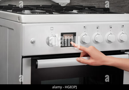 L'activation de main de femme cuisine cuisinière à gaz blanc sur fond gris Banque D'Images