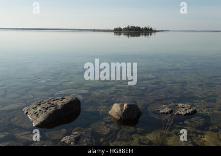 Image de calme plat, peu profond du lac Huron et de l'eau claire les roches calcaires avec petite île recouvert d'arbres sur l'horizon Banque D'Images