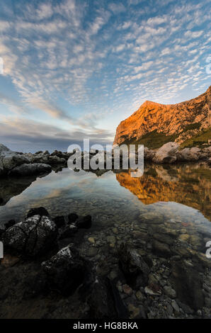 Beaux nuages épars au coucher du soleil à Barcarello, avec le promontoire de Capo Gallo reflétée sur l'eau calme. Palerme, Sicile. Banque D'Images