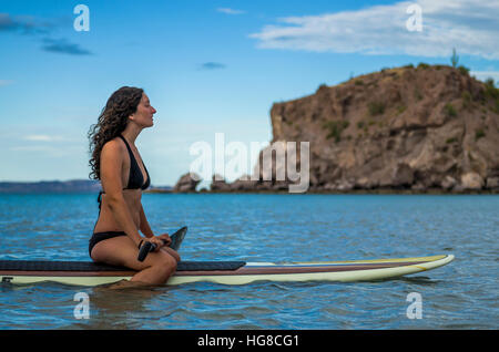 Femme assise sur la mer en paddleboard against sky Banque D'Images