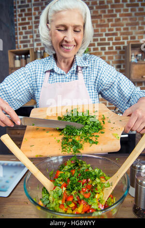 Smiling senior woman cutting salade de légumes verts Banque D'Images